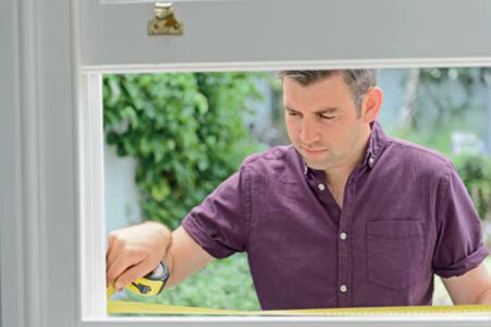 man standing at an open window using a measuring tape across it